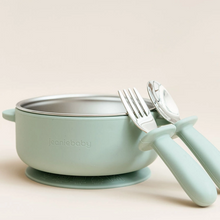 Load image into Gallery viewer, A light mint green baby bowl with a stainless steel interior and a matching silicone suction base, shown with a fork and spoon that have matching mint green handles on a warm beige background. The brand name 'jeaniebaby' is embossed on the front of the bowl.